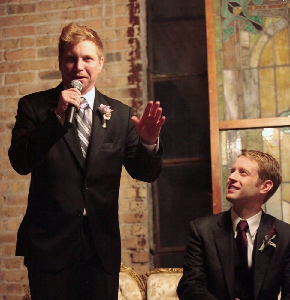 Best man giving speech at a wedding with groom sitting next to him